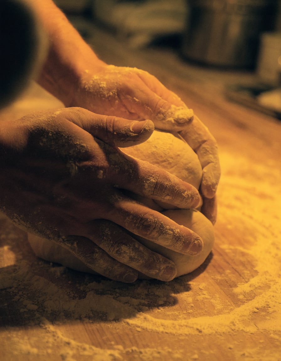 Hands shaping bread dough on a floured bench