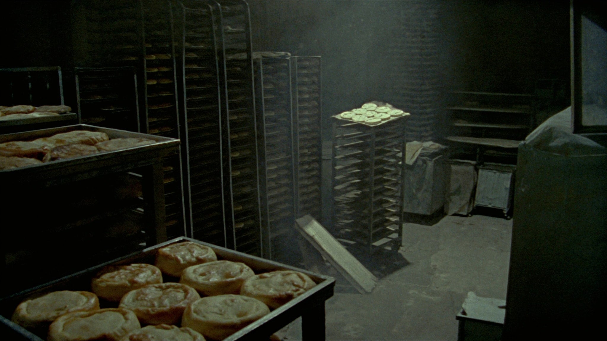 Bakery racks loaded with cooling flatbread under a single overhead work light